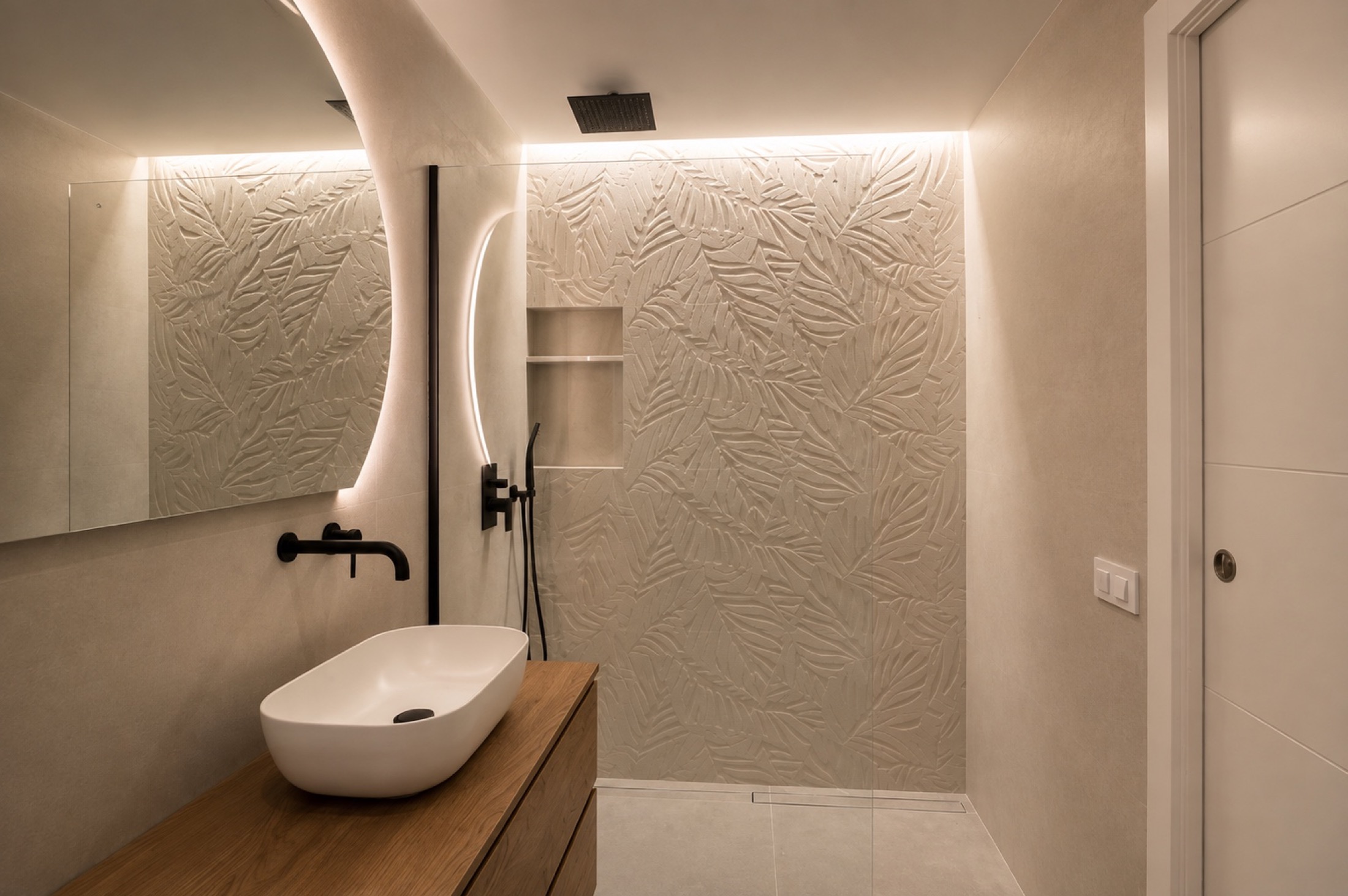 Relieve botánico. El relieve de hojas recorre la pared de la ducha. El mueble de madera y el lavabo blanco dejan que esa textura sea la protagonista.
