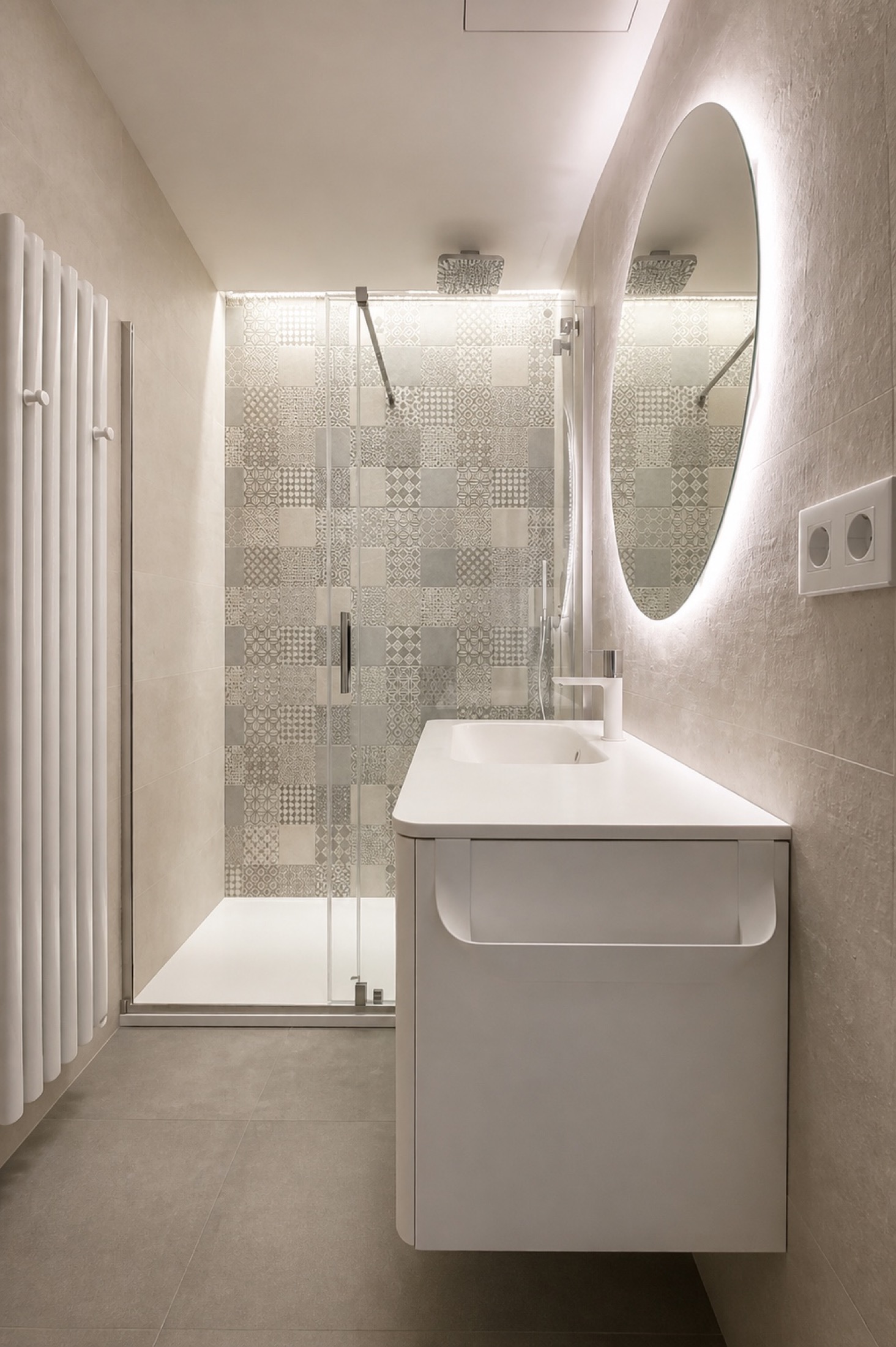 Blanco y curvas. El mueble de esquinas redondeadas y el espejo circular suavizan un baño alargado. La ducha se sitúa al fondo, junto al revestimiento de relieve.