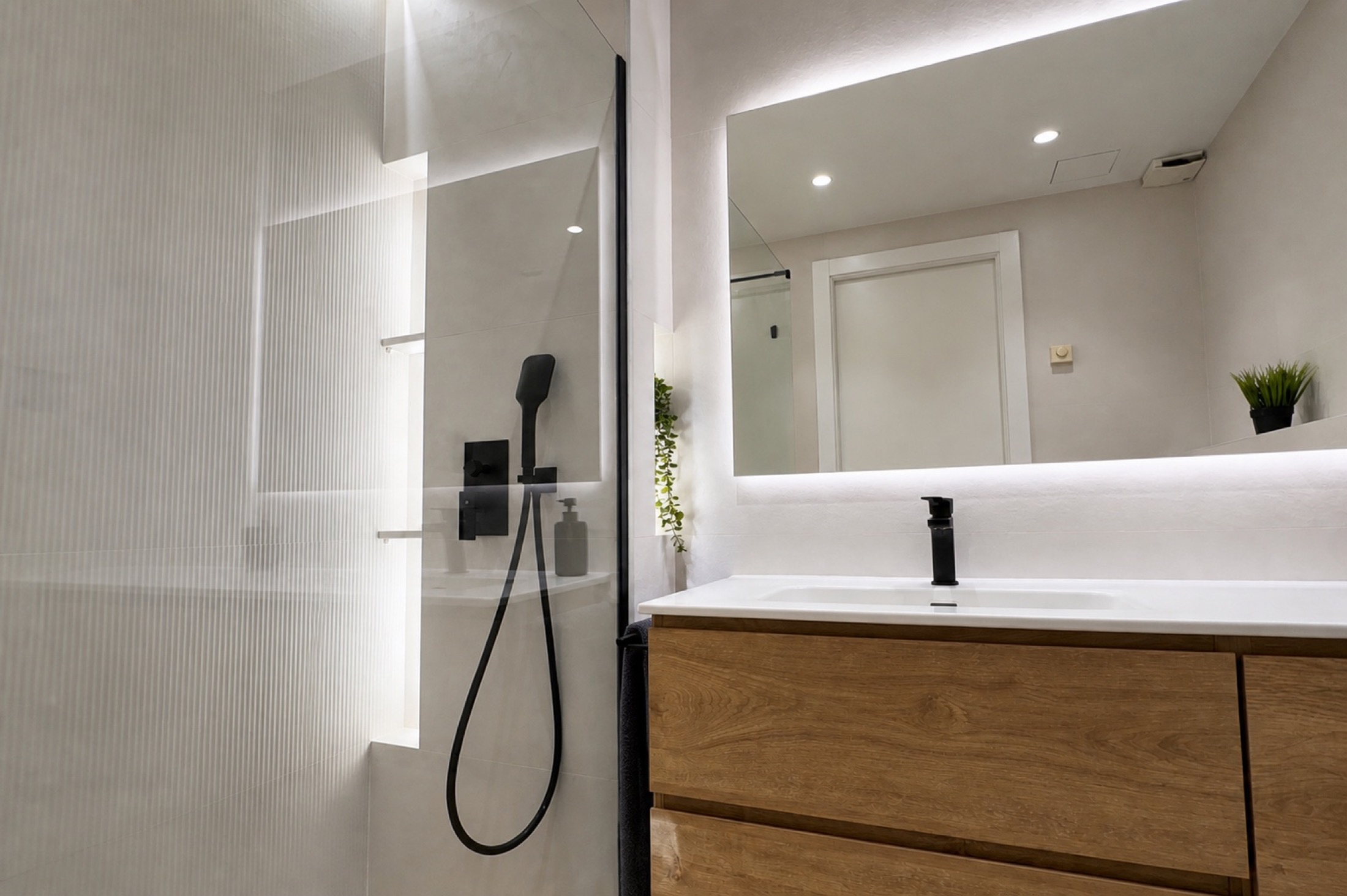 Roble sobre blanco. El mueble de madera destaca sobre los revestimientos claros. La iluminación del espejo y las hornacinas ayuda a separar las distintas zonas.