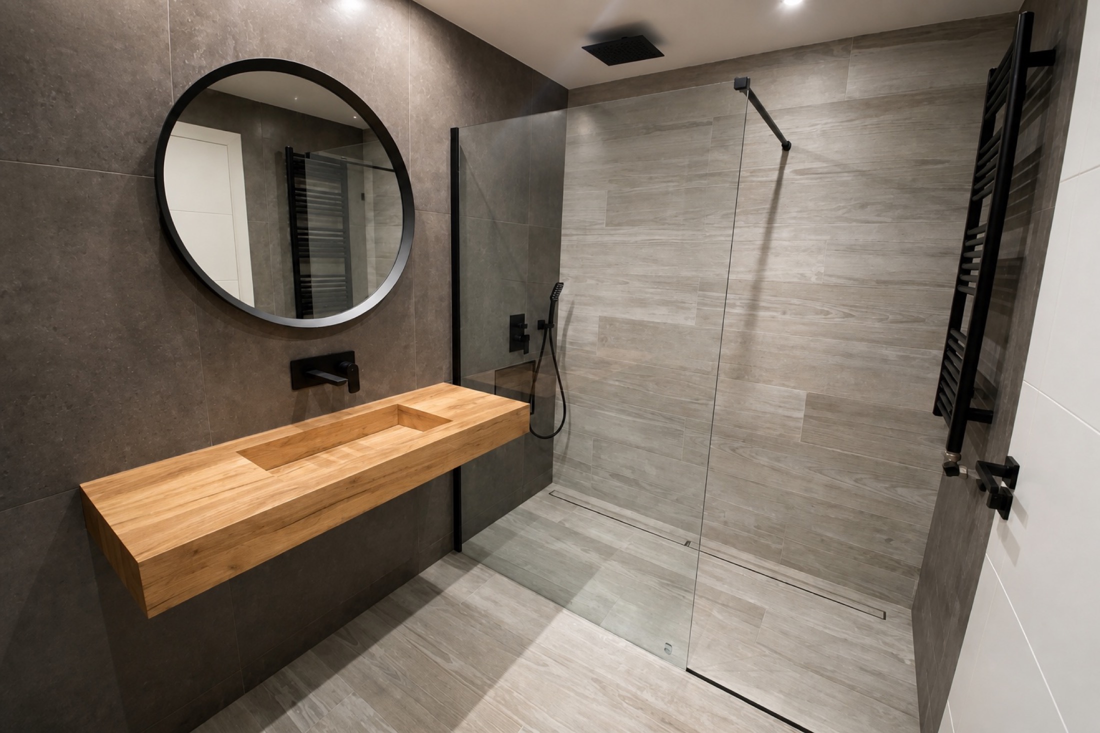 Lavabo en voladizo. Una encimera de madera suspendida y un espejo de marco negro definen el lavabo. La mampara deja a la vista la ducha y su revestimiento.