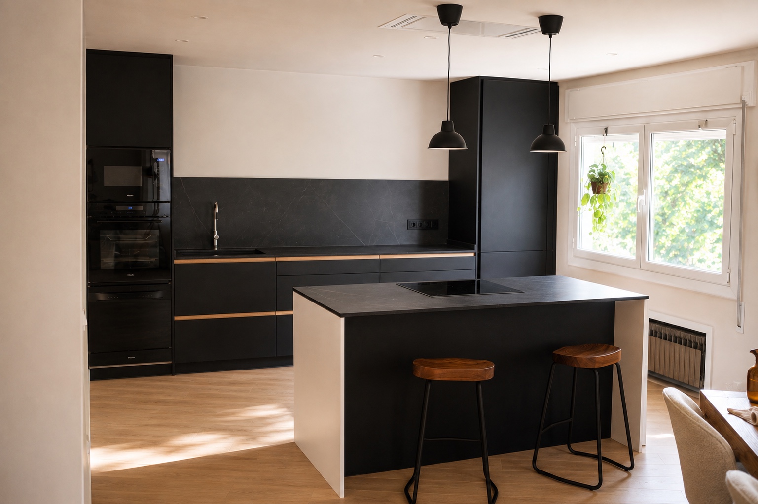 Negro y luz natural. Los muebles negros enmarcan una península con asientos. La ventana y la apertura al comedor equilibran los tonos oscuros.
