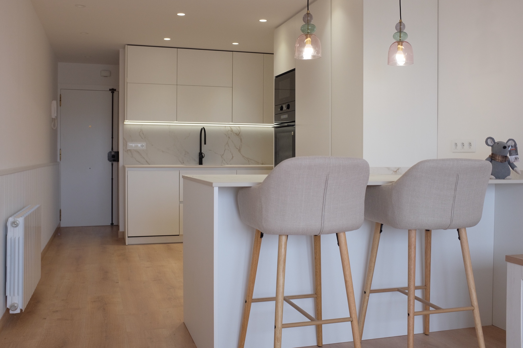 La península. Una península con taburetes sirve de apoyo a la cocina y de mesa informal. Los muebles claros aprovechan la pared hasta el techo.