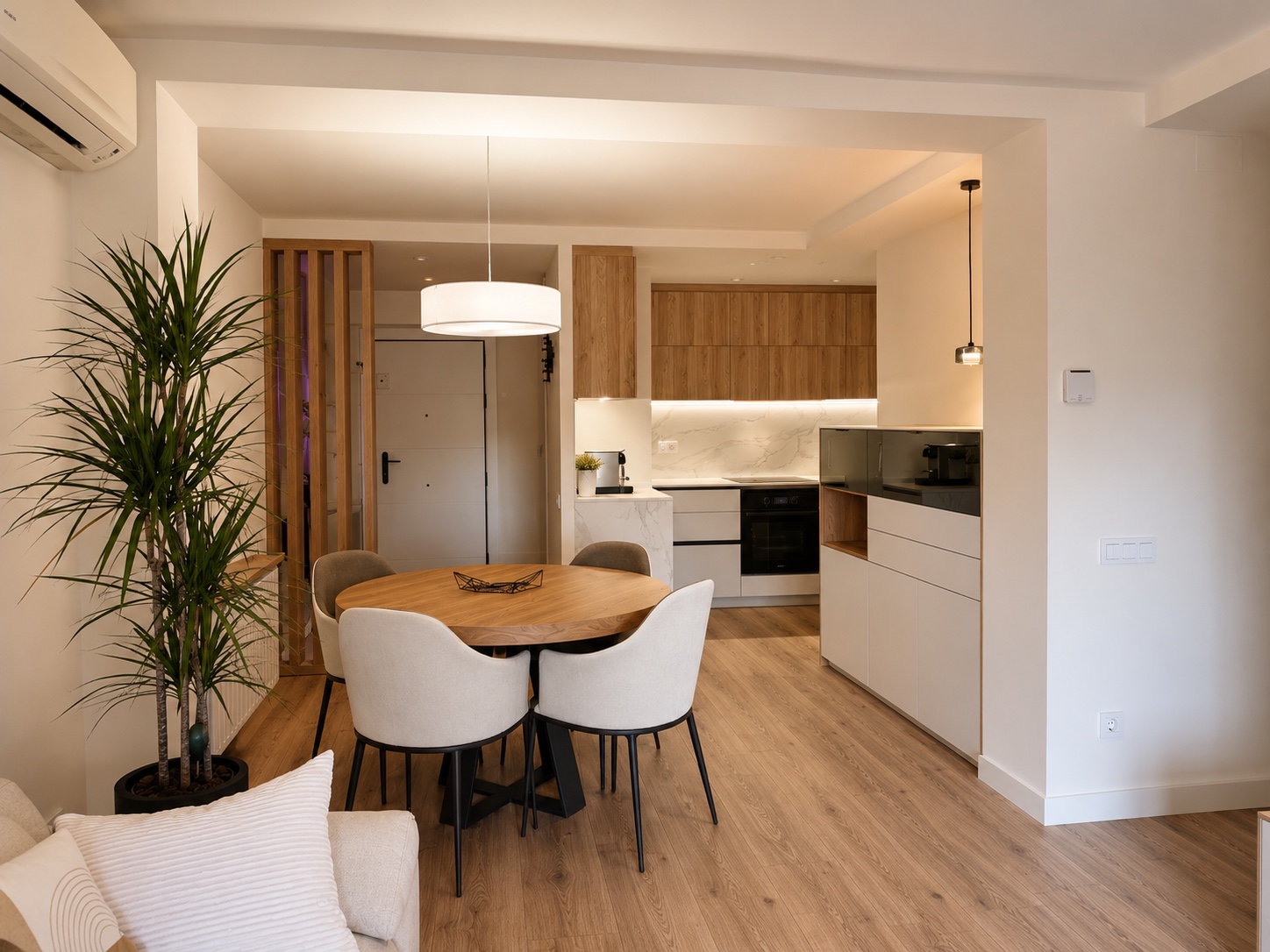 Una cocina para compartir. La mesa redonda une la cocina con el salón. El blanco y la madera se mantienen en ambos espacios, sin tabiques que los separen.